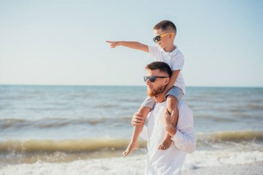 Mutlu genç baba yazın sahilde boynu çok sevimli küçük oğlunu taşıyor.