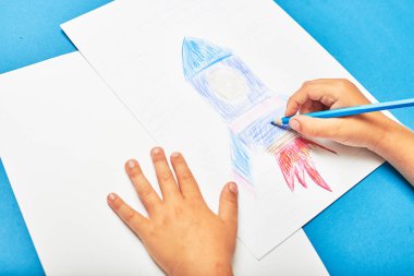 Küçük çocuk masada kalemle roket çiziyor.