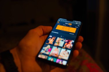 Akıllı telefon tutan ve porno sitesine göz gezdiren kişinin kırpılmış görüntüsü