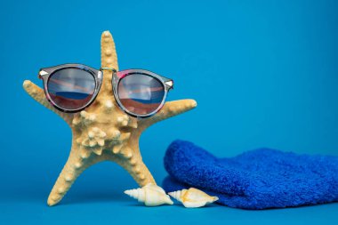 Yakın plan deniz yıldızı, güneş gözlüğü ve deniz kabuğu manzarası ve mavi arka plan havlusu, tatil konsepti  