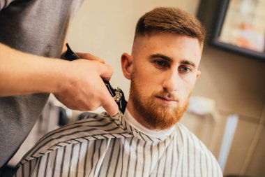 Usta berber dükkanında saç ve sakal kesiyor, kuaför genç bir adam için saç stili yapıyor.
