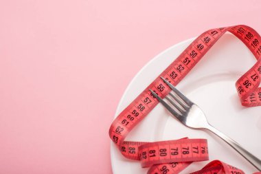 Pembe zemin üzerinde çatal ve mezurayla beyaz plakanın yakın plan görüntüsü