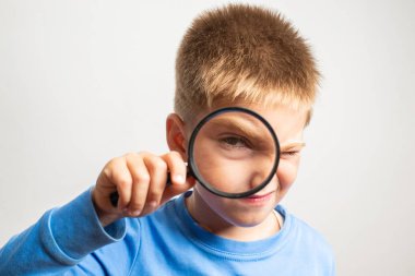 Sevimli küçük çocuk elinde büyüteçle kameraya bakıyor.