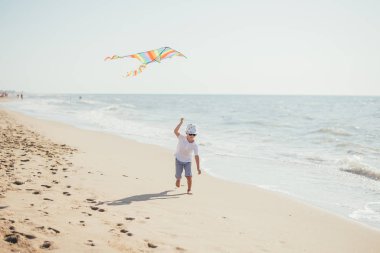Sevimli çocuk kumsalda renkli uçurtmayla oynuyor.
