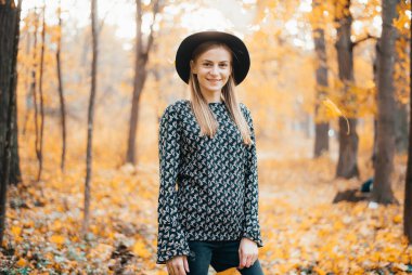 Güz ormanında duran şapkalı güzel bir kadın.
