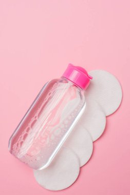 Micellar cleansing water and cotton discs to remove cosmetics and cleanse the skin on pink background clipart