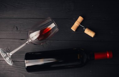 Şarap şişesinin üst görüntüsü, kırmızı şaraplı bardak ve ahşap kaplamalı tirbuşon.