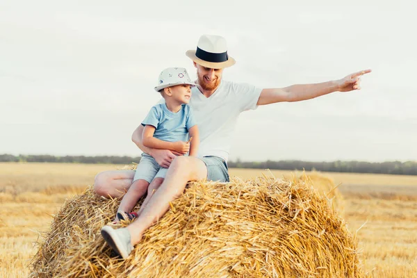 快乐的父亲和儿子坐在田里的草堆上 — 图库照片