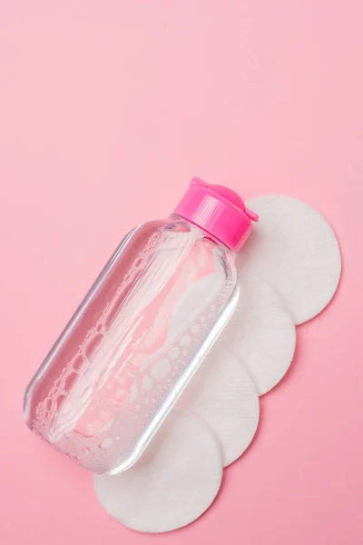 Kozmetikleri çıkarmak ve pembe arka plandaki deriyi temizlemek için Micellar 'ın temizleme suyu ve pamuk diskleri