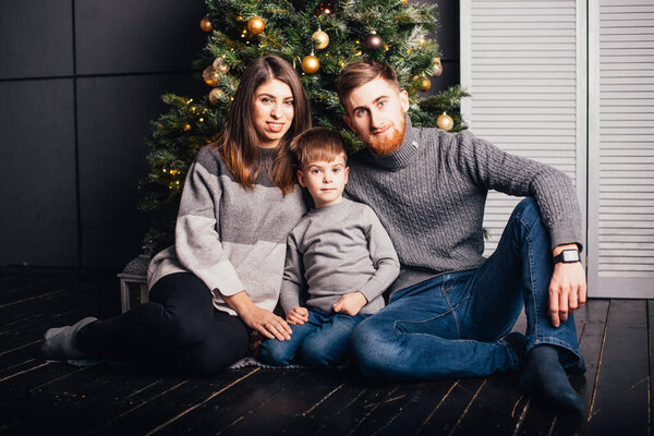 happy young family with one child sitting together near christmas tree and smiling at camera