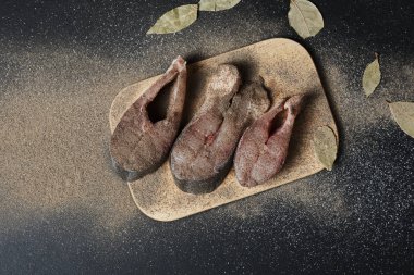 Baharatlı ve defne yapraklı lezzetli balıkların siyah yüzeydeki ahşap tahtada yakın plan görüntüsü.