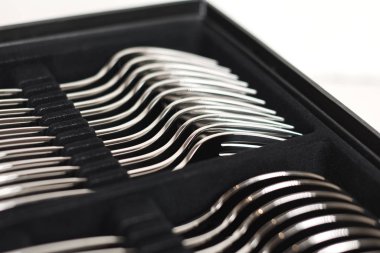 Beyaz arkaplanda siyah kabın içindeki parlak çatal bıçak takımının yakın plan görüntüsü 