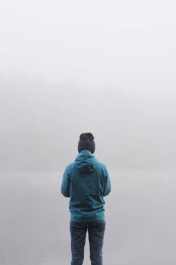 Sisli bir sabahta nehrin kenarında duran genç kadının arka görüntüsü.
