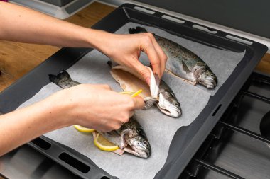 Bir kadının taze balığı limon dilimleri ve baharatlarla pişirme tepsisinde hazırlarken çekilmiş bir fotoğrafı.