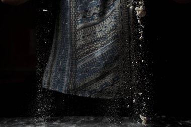 Kırpılmış bir kadın un seçerken ve siyah arka planda hamur yaparken.