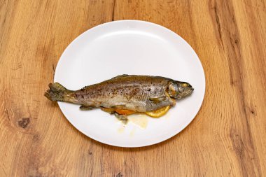 Tahta masadaki beyaz tabakta limonlu lezzetli fırında balık manzarası.