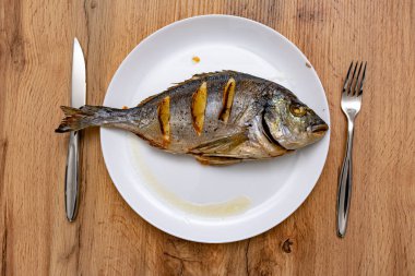 Limon dilimleri, çatal ve bıçakla ahşap masada nefis pişmiş balık manzarası.