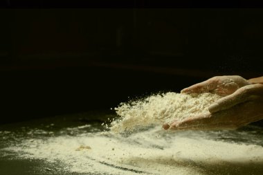 Kırpılmış bir kadın un seçerken ve siyah arka planda hamur yaparken.