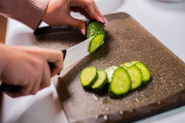 Sağlıklı salata için taze salatalık doğrayan bir kadın resmi.  