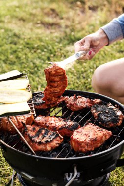 Kömür ızgarasında nefis et pişiren bir kadın resmi.  