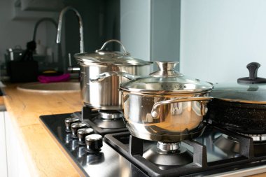 Modern mutfaktaki ocağın üzerinde parlak tavalar ve çatal bıçaklar.