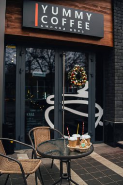 Kahve dükkanının yanındaki masada tek kullanımlık kahve fincanları ve zencefilli kurabiye var.