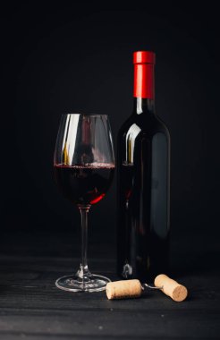 Şarap şişesinin yakın plan görüntüsü, bir kadeh kırmızı şarap ve ahşap arka planda tıpası olan tirbuşon.