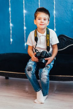 Küçük sevimli çocuk elinde dijital kamerayla oturmuş kameraya gülümsüyor.