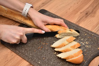 Tahta masada bıçakla taze ekmek kesen bir kadın resmi.