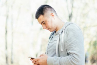 side view of handsome focused young man standing and using smartphone outdoors