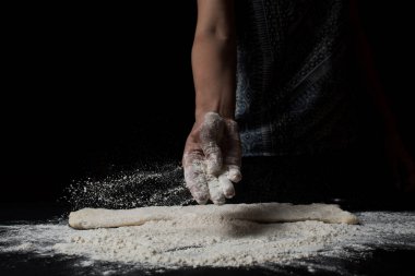 Kadının un ellerken ve siyah arka planda taze ev yapımı hamur pişirirken kısmi görüntüsü