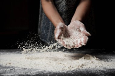 Buğday unu karıştıran ve siyah arka planda hamur yapan bir kadın.