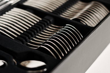 Beyaz arkaplanda siyah kabın içindeki parlak çatal bıçak takımının yakın plan görüntüsü 