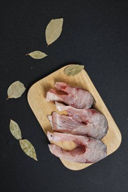 Tahta tahtada siyah arka planda defne yapraklı balık dilimlerinin üst görüntüsü