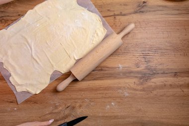 Ahşap masada merdaneyle hamuru hazırlayan kadının kısmi görüntüsü 