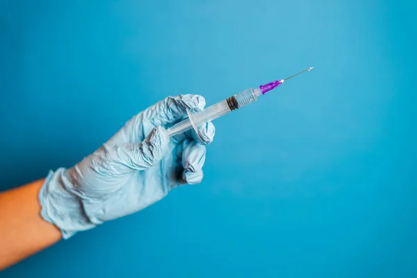 Cropped shot of doctor in glove holding syringe with vaccination on blue background. Liquid medication or drug