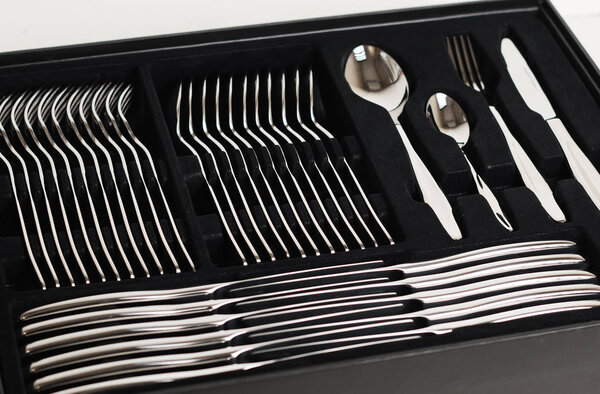 Крупный план блестящих серебряных столовых приборов в черном контейнере на белом фоне
