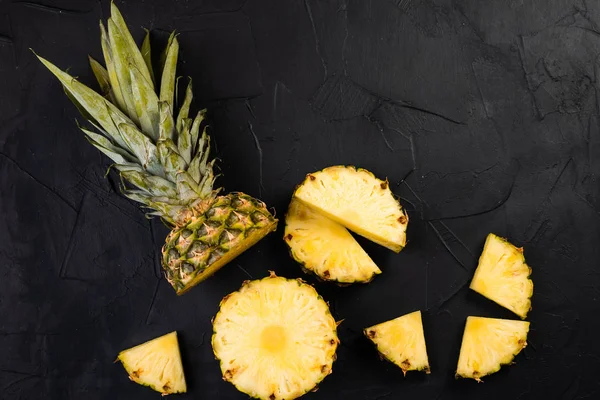 top view of fresh sliced pineapple on wooden board on black background