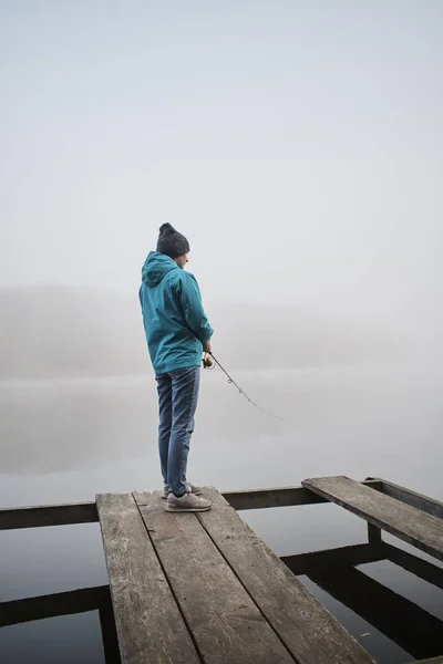 木製の桟橋に立つ若い女性と霧に包まれた朝のロッドで釣る姿を — ストック写真
