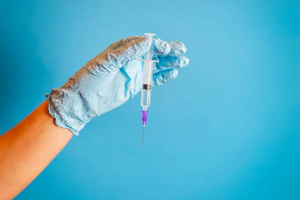 Cropped shot of doctor in glove holding syringe with vaccination on blue background. Syringe with injection solution. Liquid medication or drug