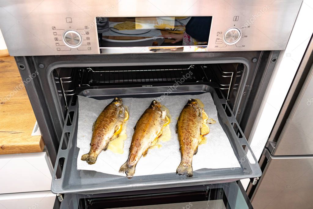 high angle view of delicious fish with lemon slices cooking on baking tray in oven