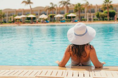 Dışarıdaki yüzme havuzunda dinlenen mayo ve şapkalı genç kadının arka görüntüsü. 
