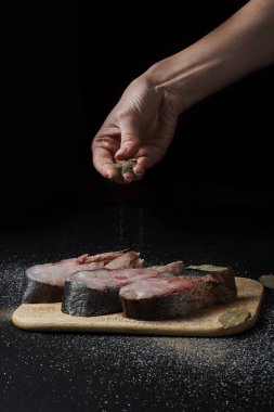 Kırpılmış bir kadın, siyah yüzeyde baharatlı ve defne yapraklı lezzetli balıklar pişiriyor.