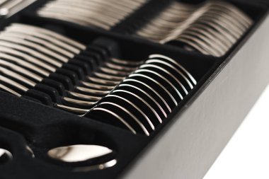 Beyaz arkaplanda siyah kabın içindeki parlak çatal bıçak takımının yakın plan görüntüsü 