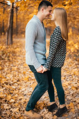 Sonbahar parkında el ele tutuşup öpüşen mutlu genç çift.