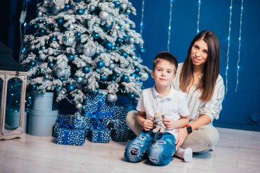 Mutlu bir anne ve küçük sevimli bir oğlu var. Noel ağacının yanında hediye kutularıyla.