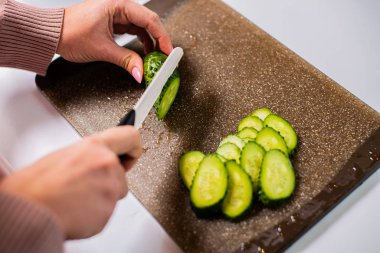 Sağlıklı salata için taze salatalık doğrayan bir kadın resmi.  