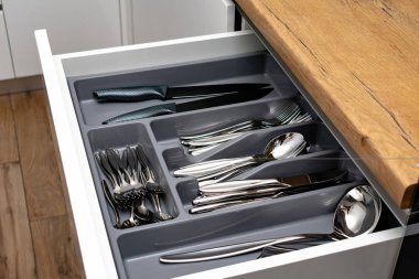 Mutfaktaki siyah kabın içindeki parlak çatal bıçak takımı koleksiyonu, yakın çekim görüntüsü.  