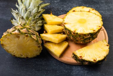 Koyu arkaplanda tahta üzerinde taze dilimlenmiş ananasın yakın plan görüntüsü  