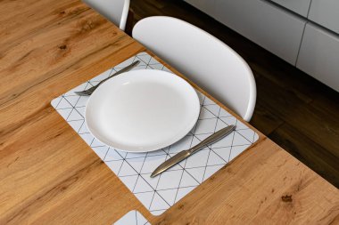 Tahta masada servis edilen çatal ve bıçaklı boş yuvarlak tabak. 